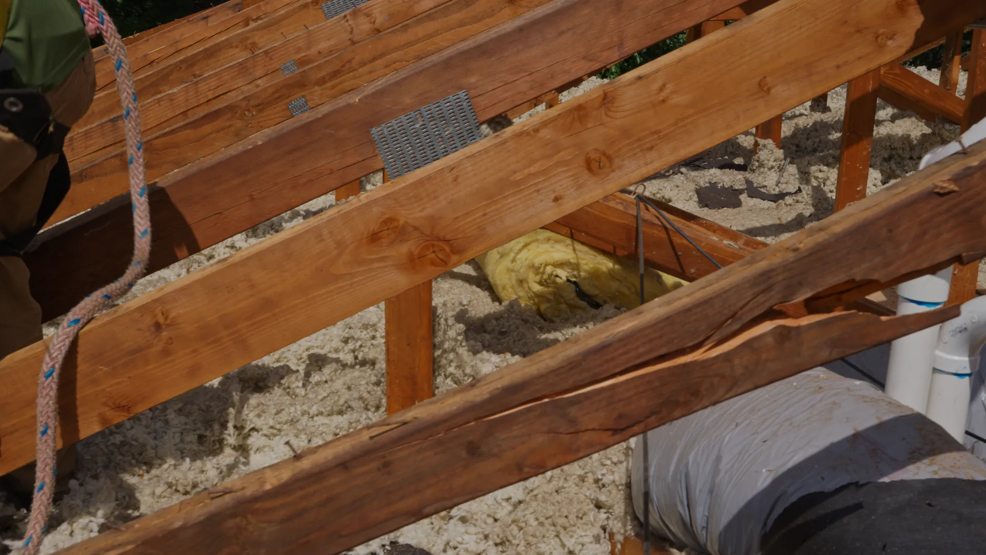 Close-up of cracked wooden roof rafters with blown-in attic insulation below, found mid-tearoff in Gladstone, OR