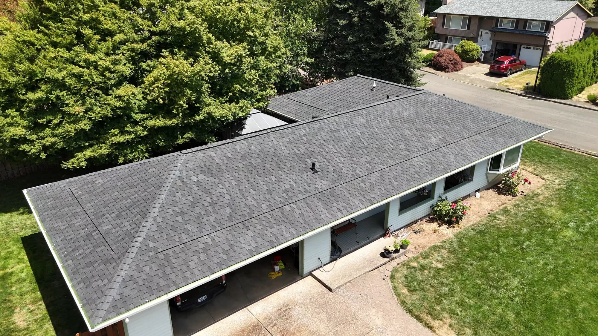 Aerial view of the back of a house showing a completed dark gray shingle roof and carport in Gladstone, OR