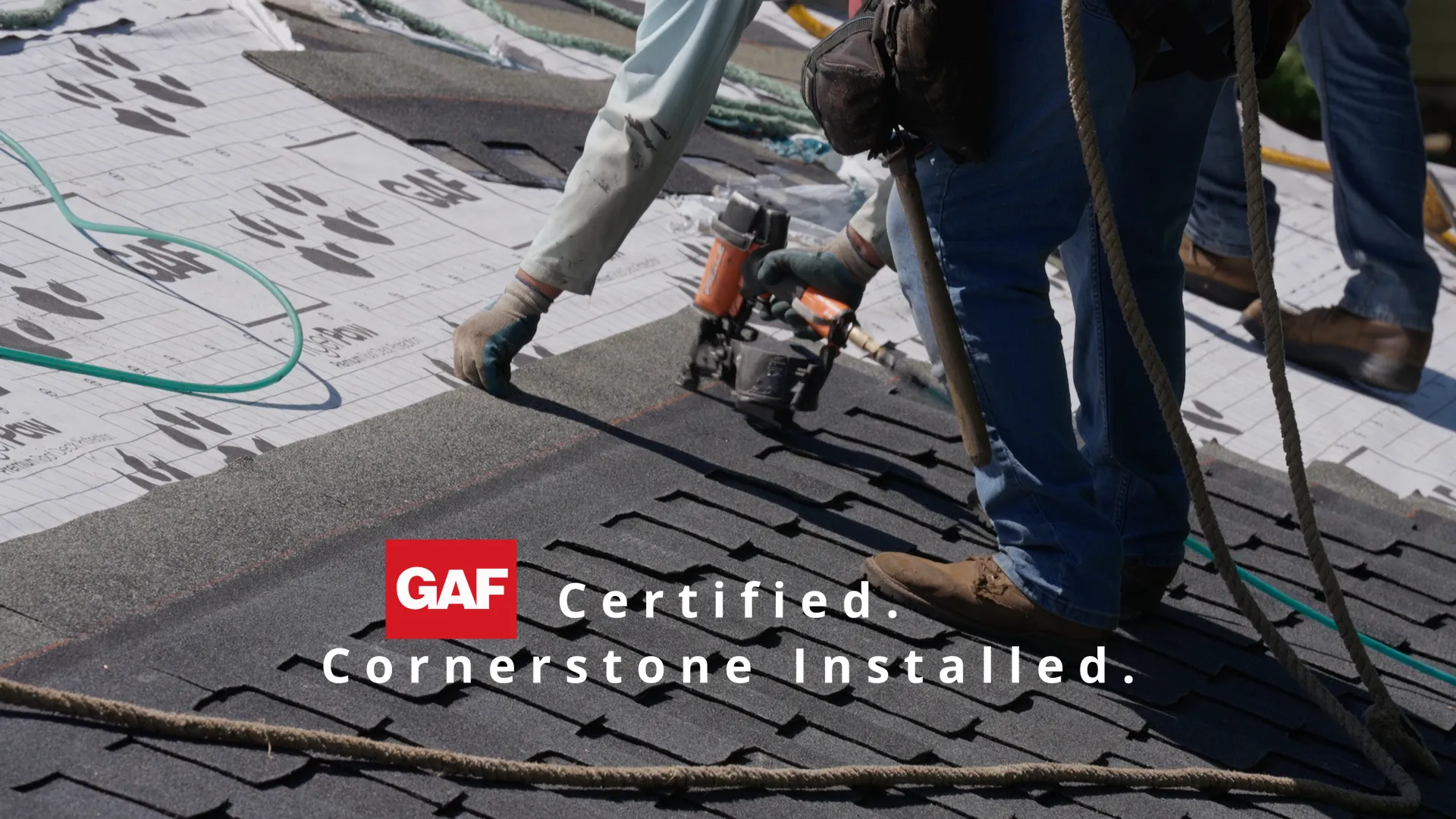 Worker fastening dark asphalt shingles over printed underlayment with a pneumatic nail gun in Gladstone, OR