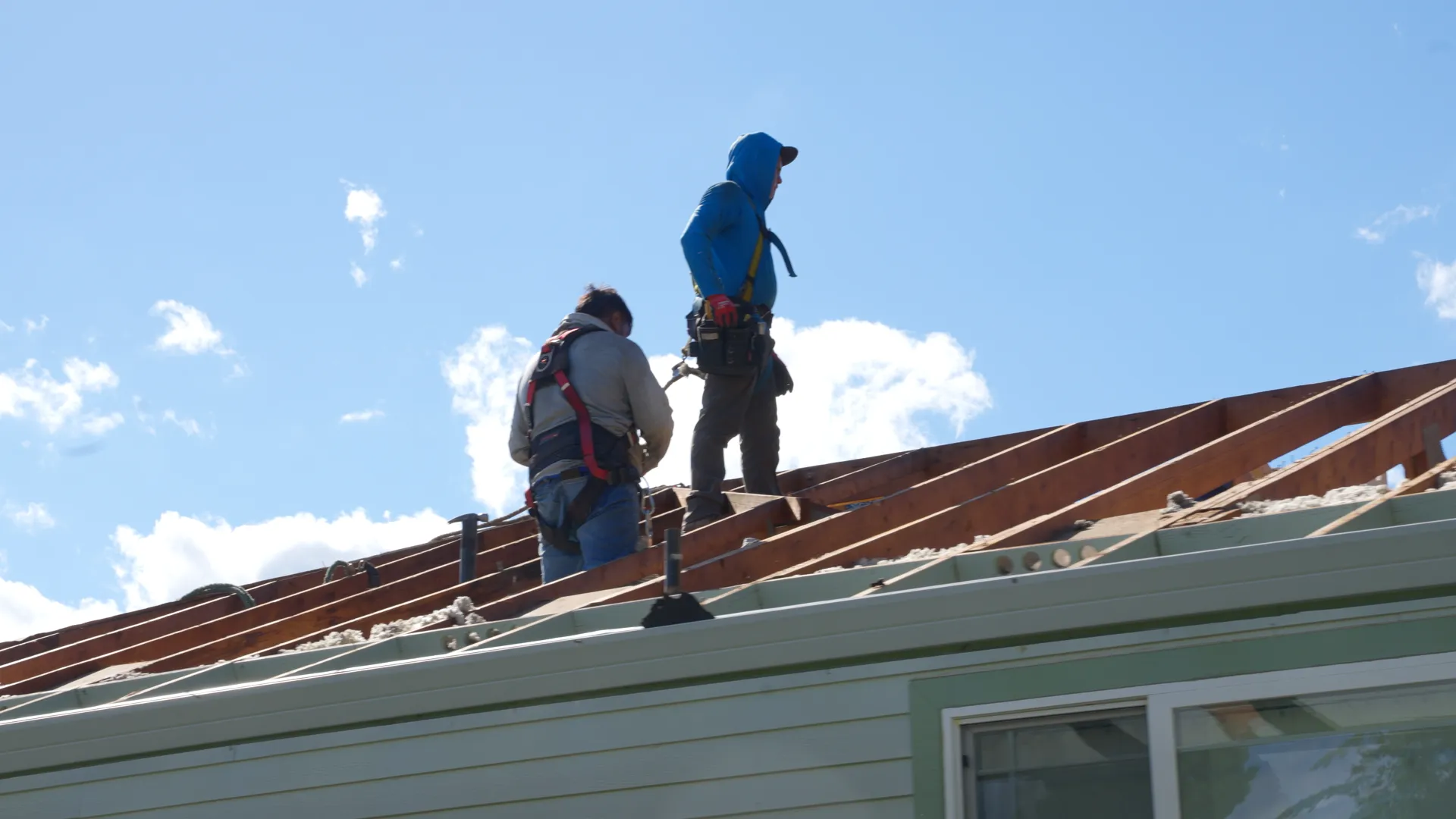 Two harnessed workers standing on exposed wooden rafters of a stripped roof in Gladstone, OR