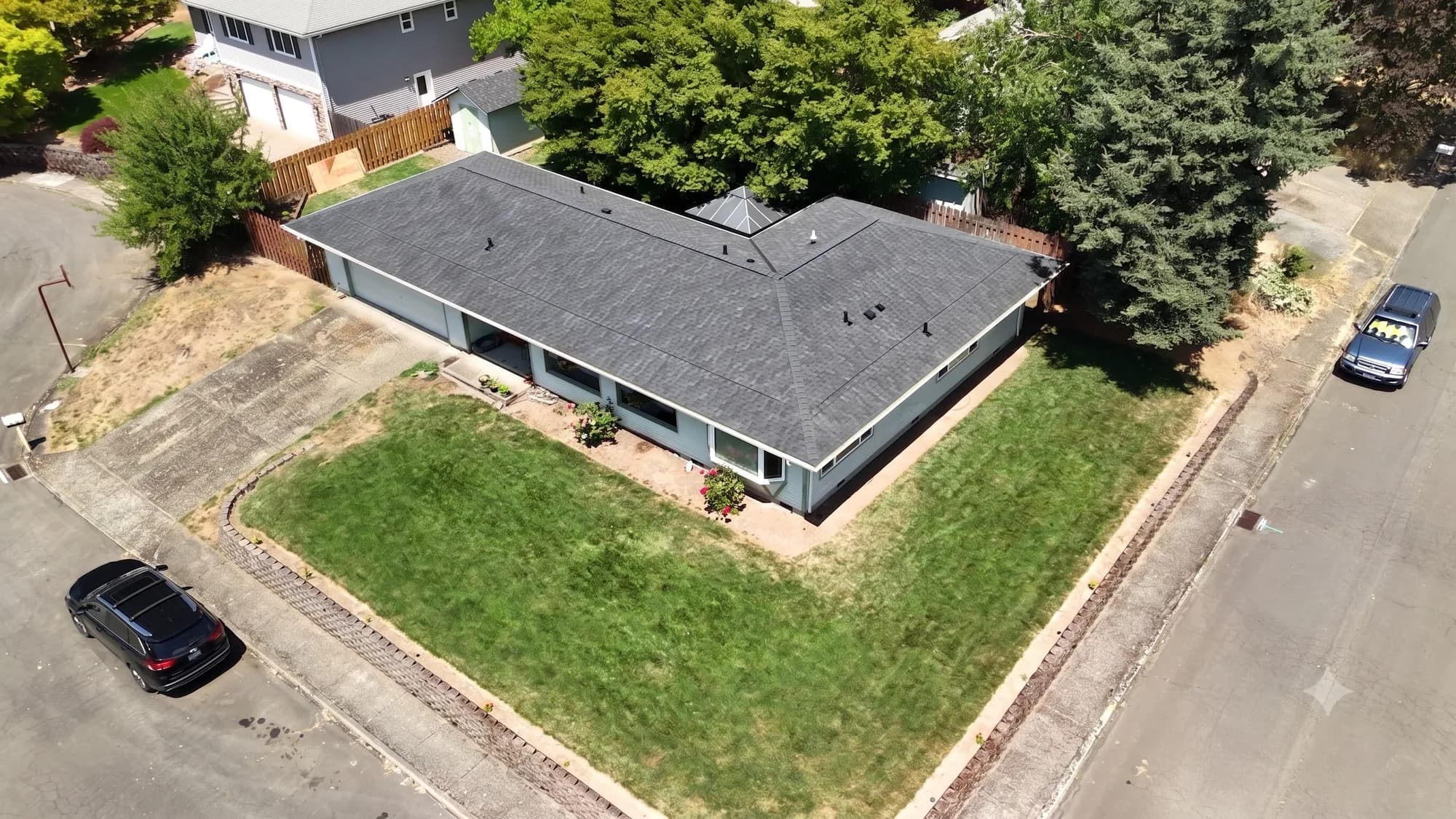 Aerial view of a completed dark gray shingle roof on a corner-lot ranch house in Gladstone, OR