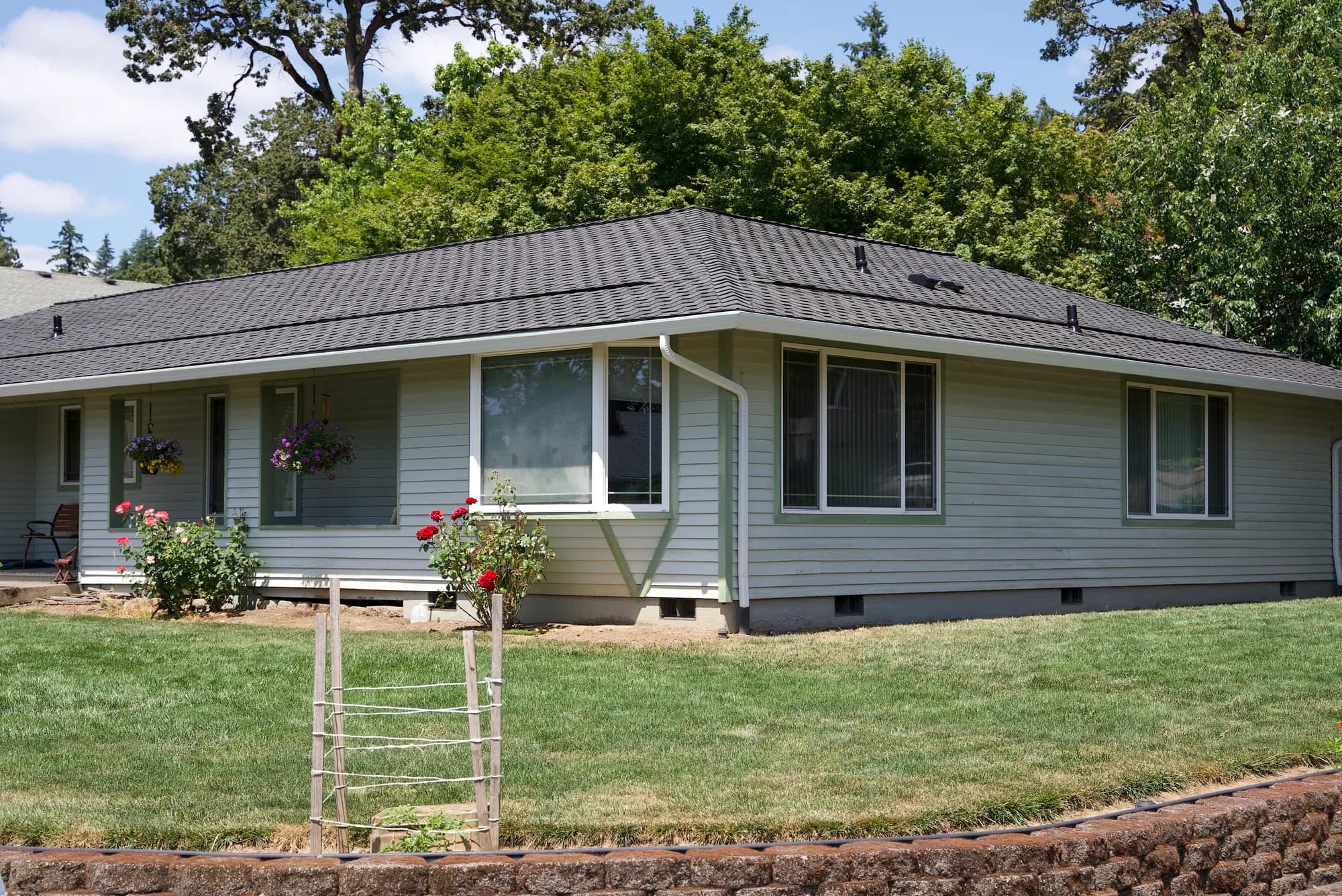 Wide front elevation of a ranch house with a dark gray shingle roof and white gutters in Gladstone, OR