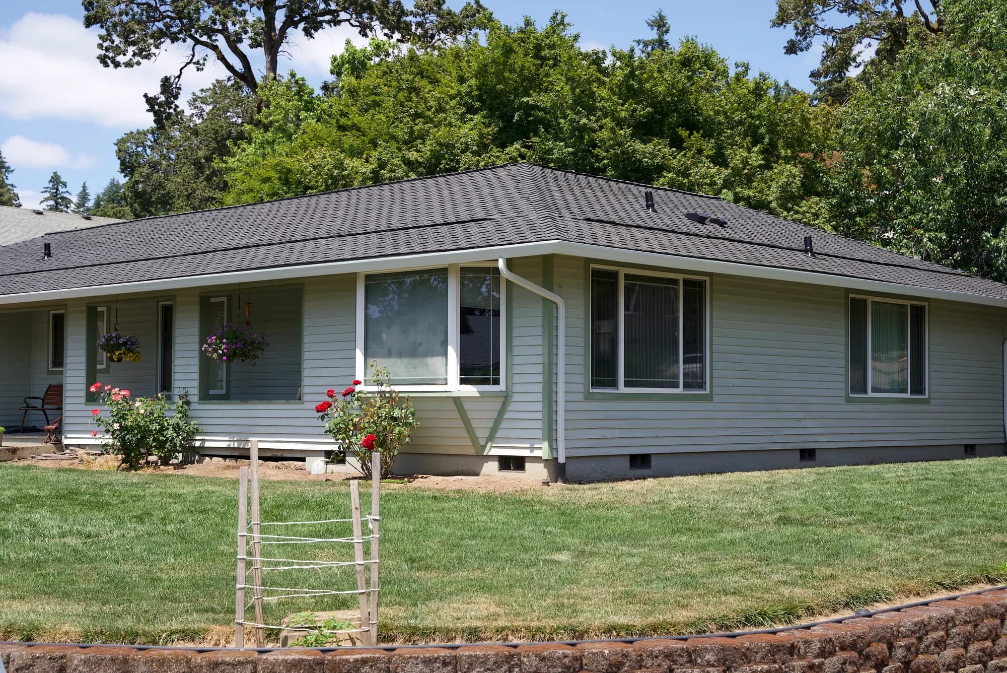 New white gutters and downspout on a Gladstone, OR ranch home with a dark gray shingle roof by Cornerstone Renovations