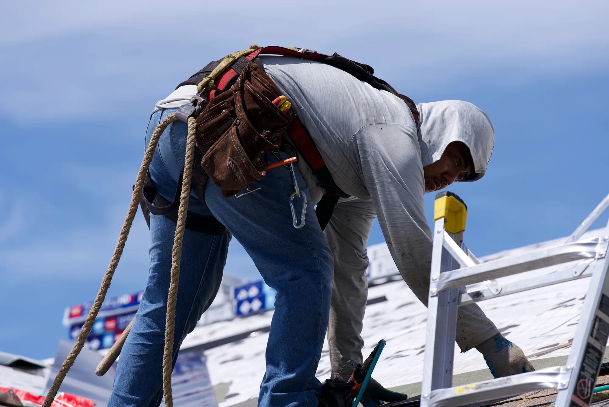A harnessed roofer working on printed underlayment with GAF shingle bundles stacked nearby in Hillsboro, OR