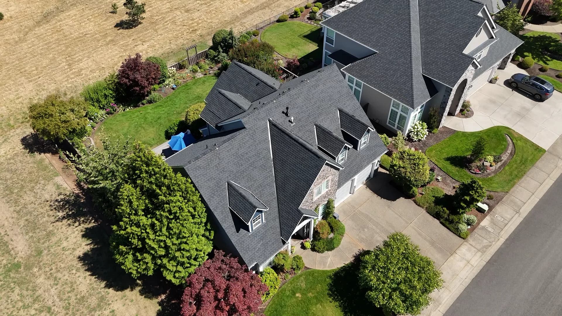 Aerial view of a two-story house with a completed charcoal shingle roof and an open field behind in Salem, OR