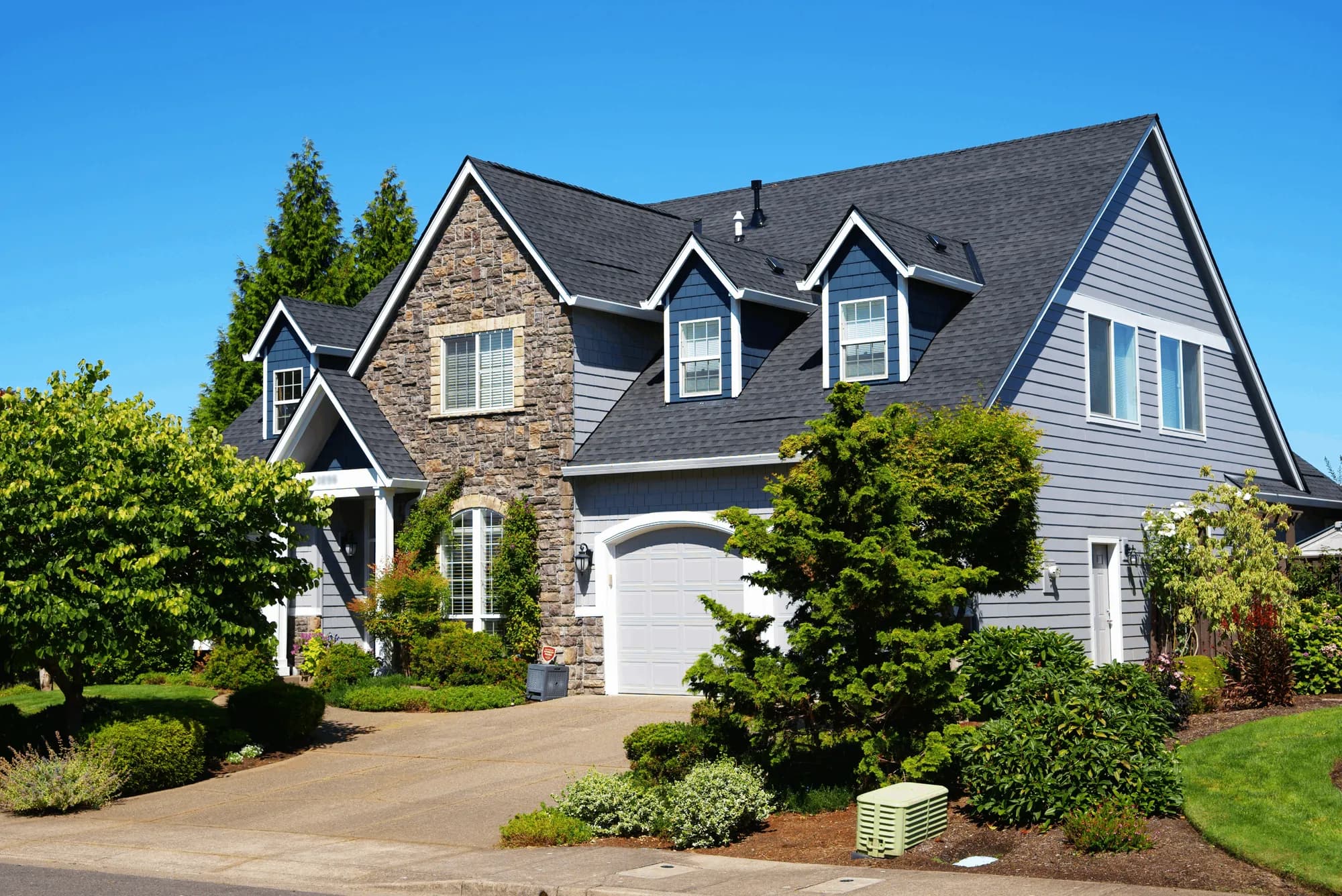 Street view of a two-story house with a completed charcoal shingle roof, stone entry gable, and dormers in Salem, OR