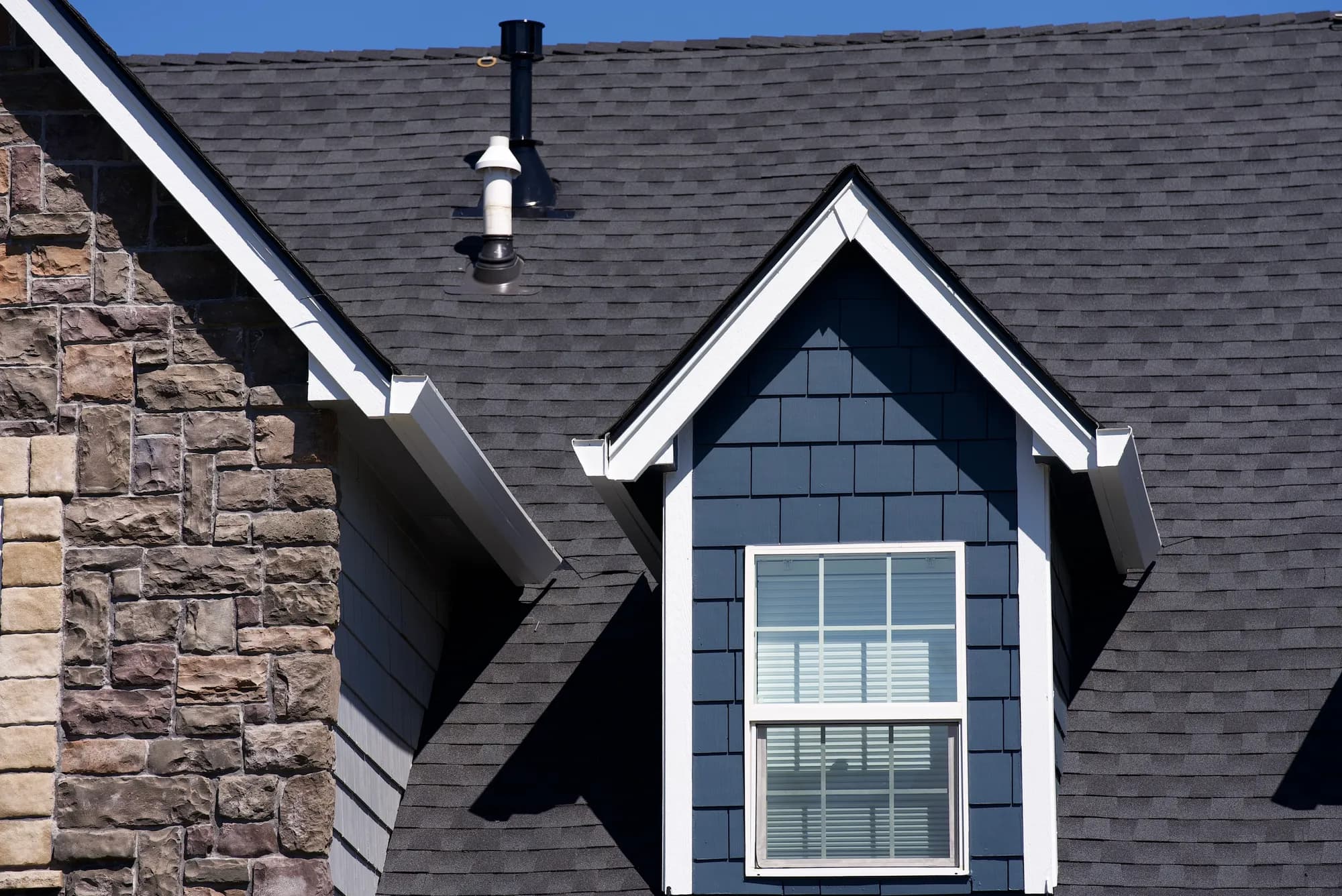 Gabled dormer with blue shake siding beside a stone chimney gable and plumbing vent on a new charcoal shingle roof in Salem, OR