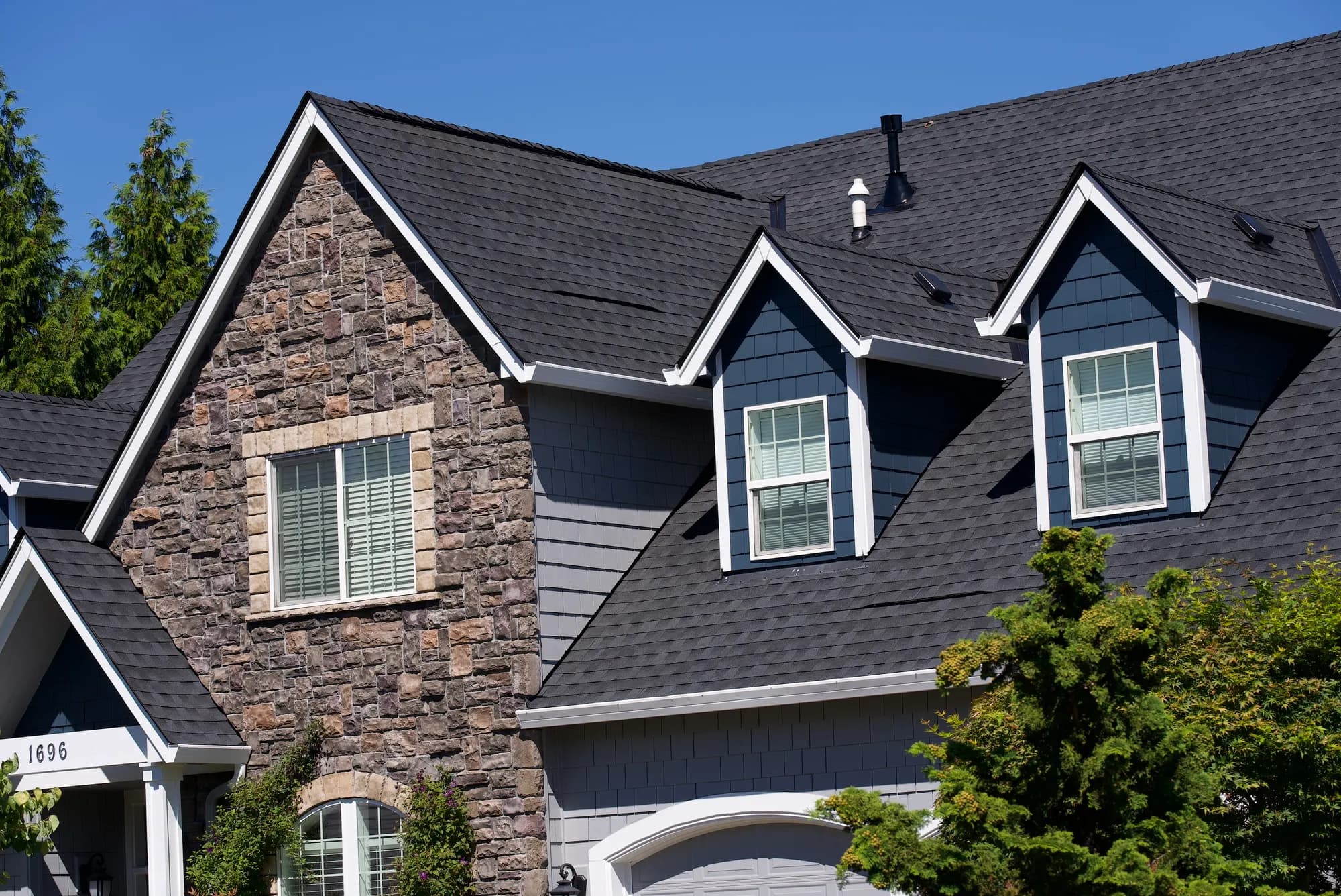 Angled front elevation showing the stone entry gable, two dormers, and garage beneath a new charcoal shingle roof in Salem, OR