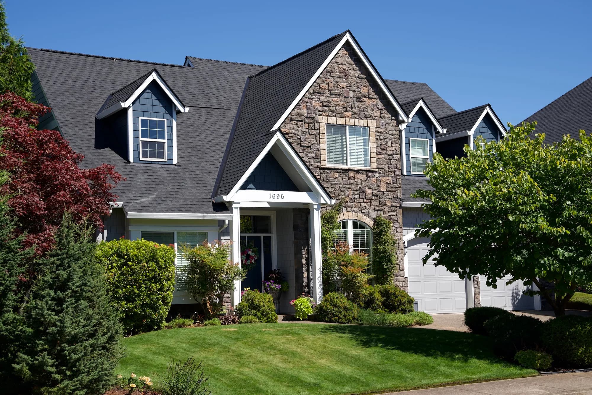 Full front elevation of a two-story house with a new charcoal shingle roof, stone entry gable, and green lawn in Salem, OR
