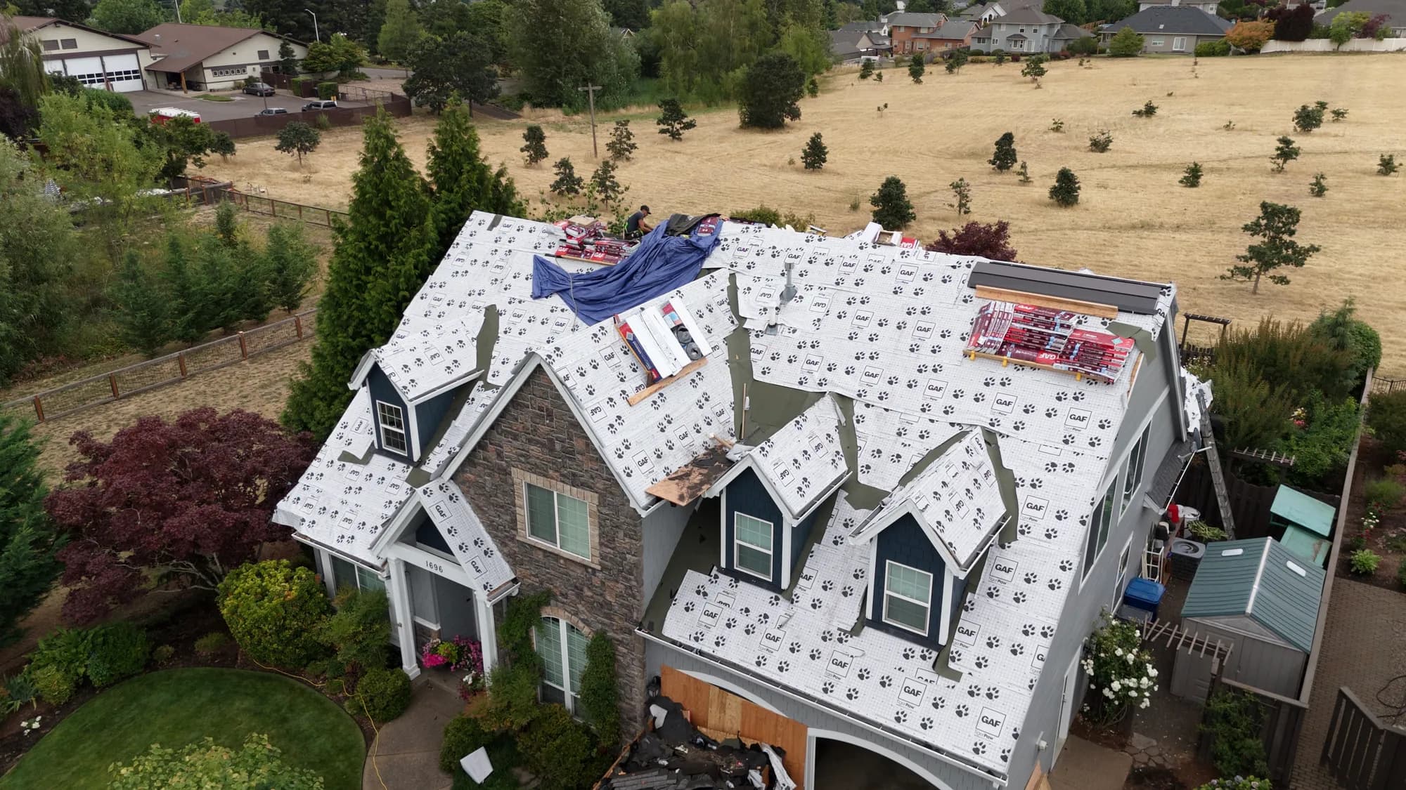 Aerial view of the front of a house mid-reroof covered in GAF Tiger Paw underlayment with bundles and a blue tarp on the roof in Salem, OR