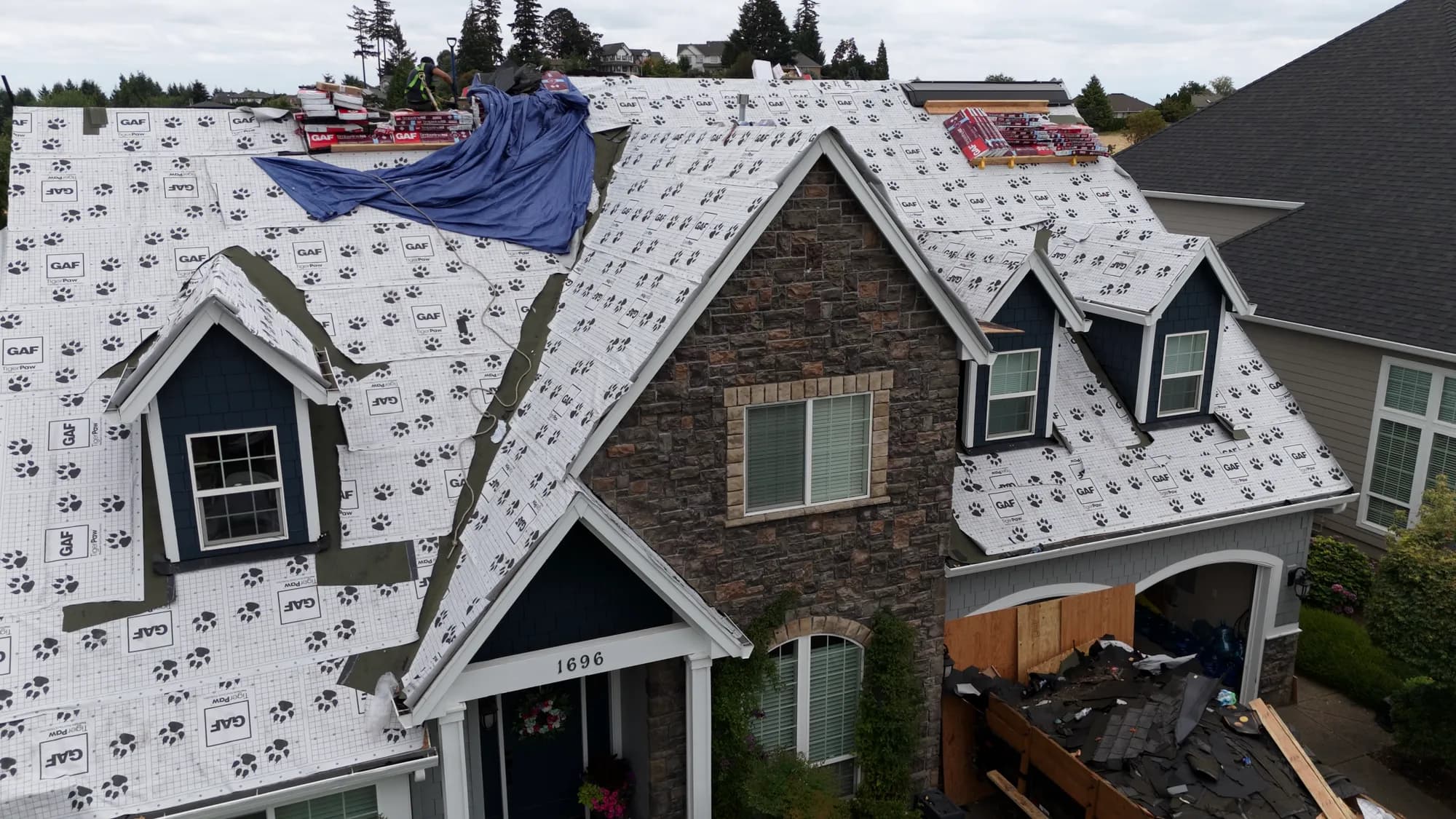 Aerial view of a Salem, OR home mid-reroof with synthetic underlayment on the roof and a dump trailer of old shingles in the driveway
