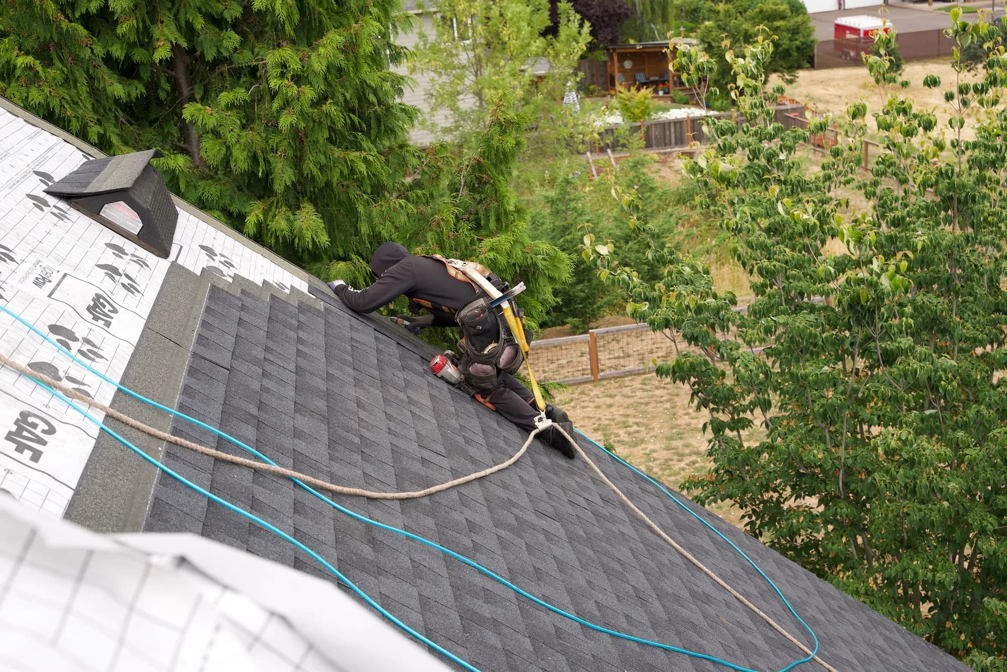 A harnessed roofer kneeling on new dark shingles at the edge of GAF Tiger Paw underlayment in Salem, OR