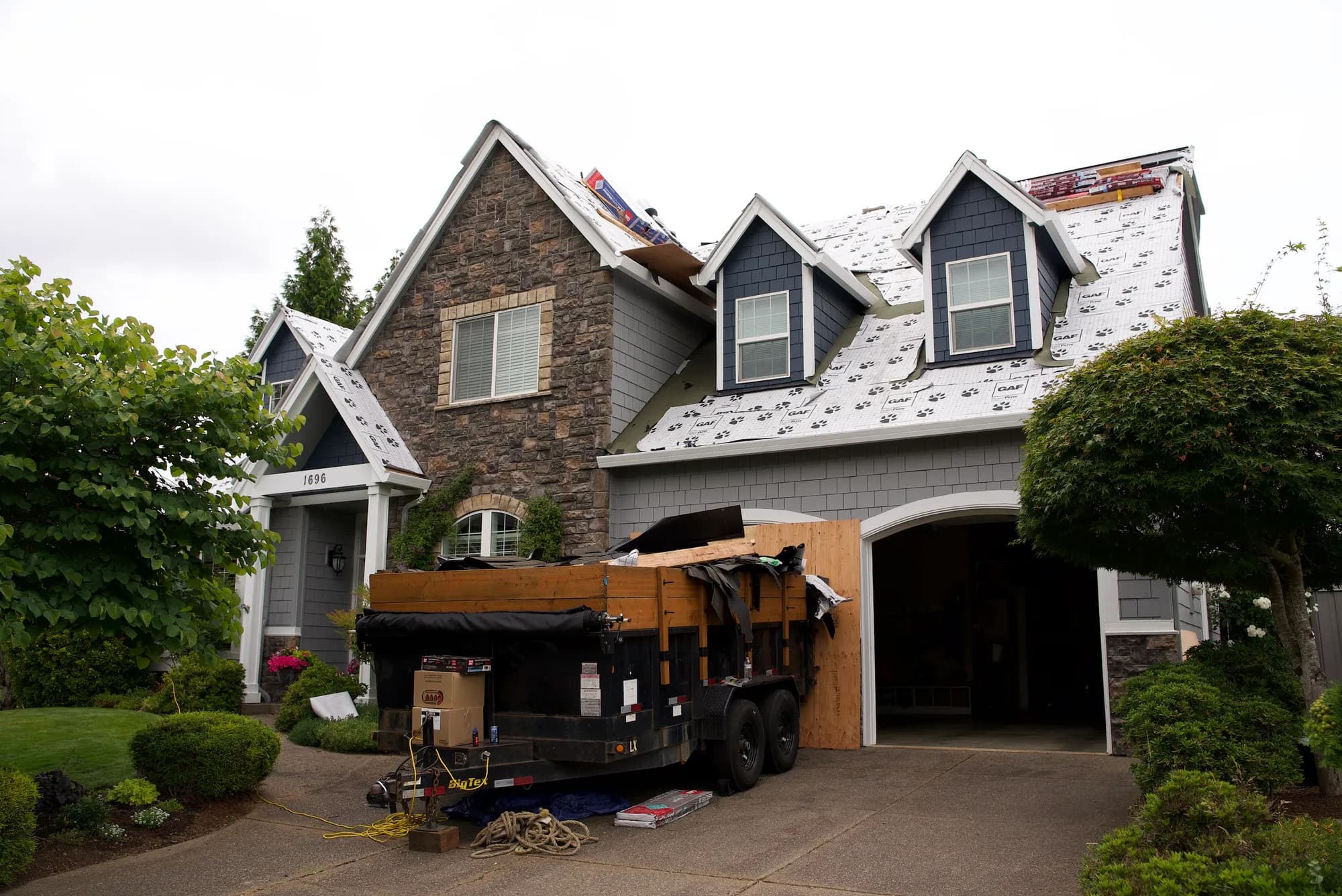 Front of a house mid-reroof with GAF Tiger Paw underlayment on the roof and a dump trailer in the driveway in Salem, OR