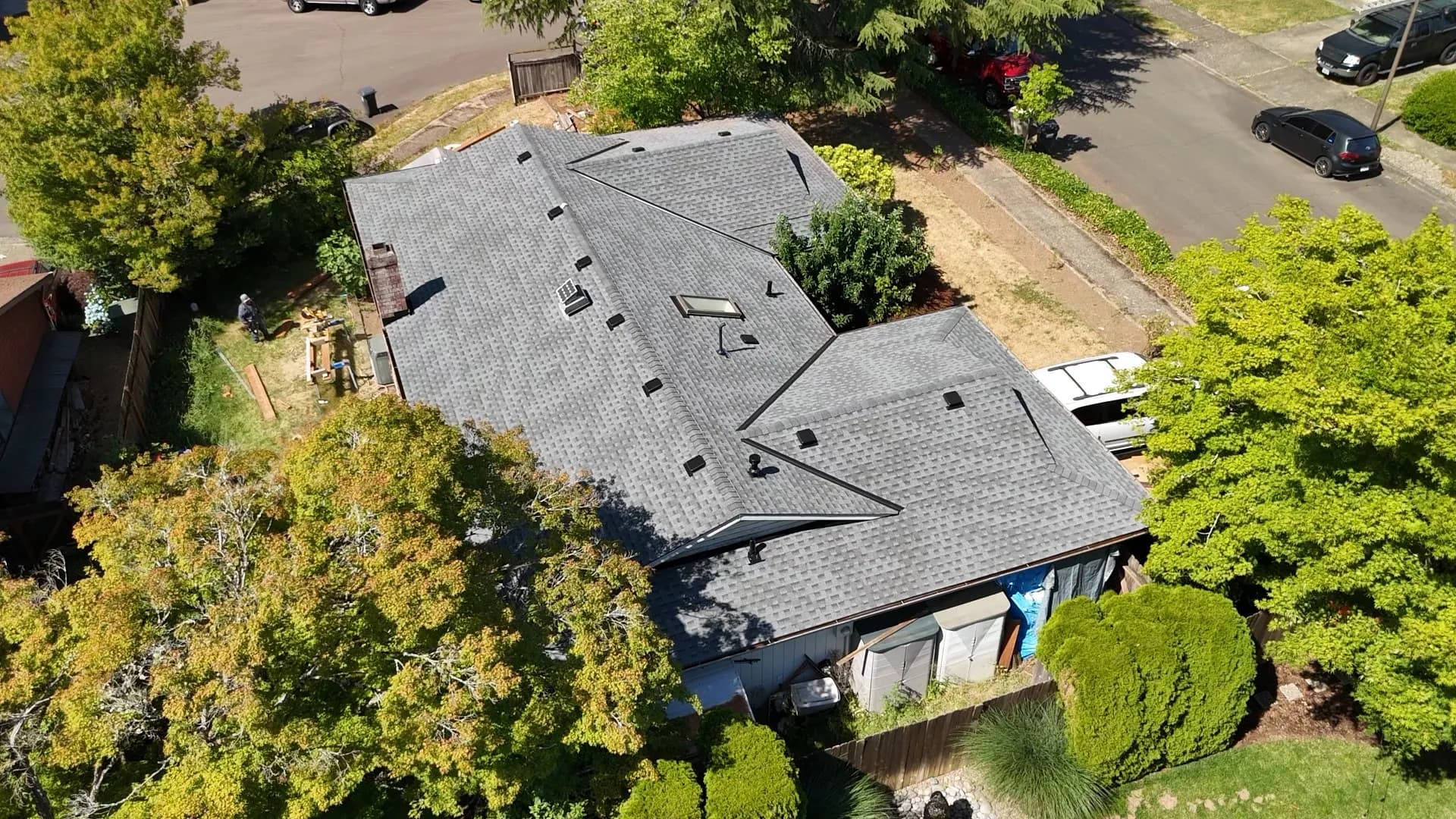 Top-down aerial view of a completed gray shingle roof with skylights and a brick chimney in Tualatin, OR