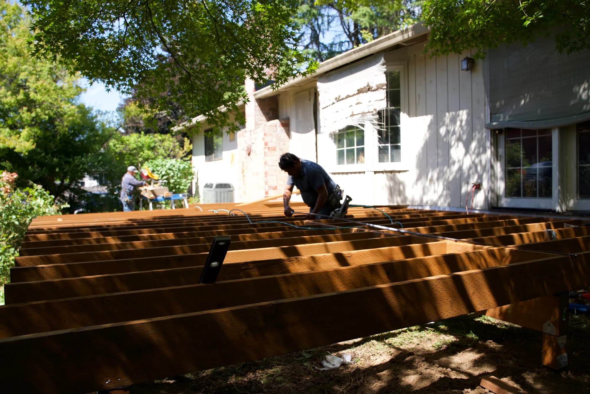 A worker leaning over wooden deck joists with a nail gun during a deck build in Tualatin, OR