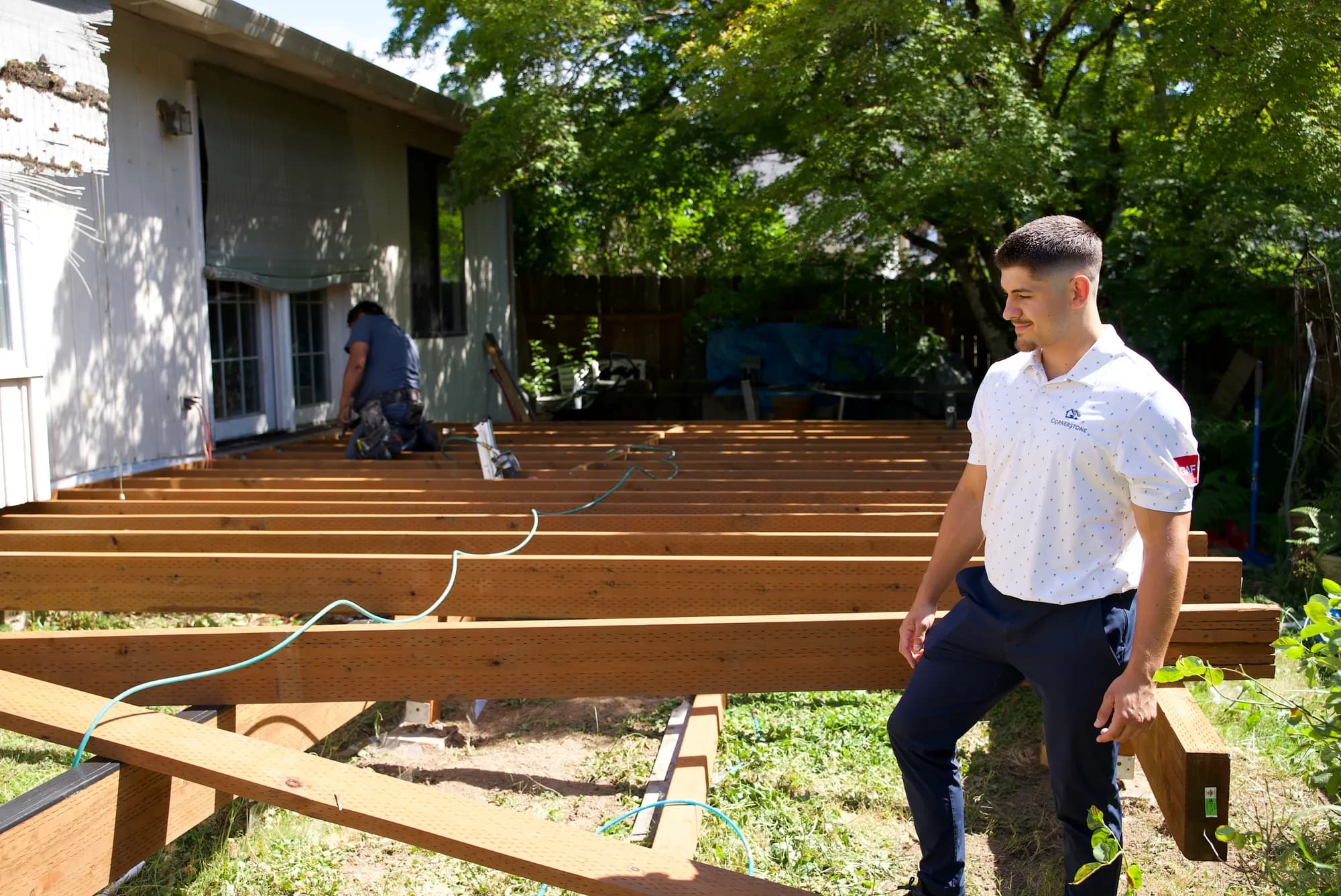 A crew member standing at the edge of a framed deck while a worker fastens joists near the house in Tualatin, OR