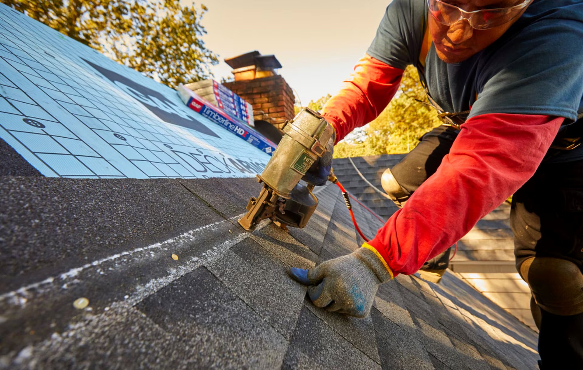 Roofer fastening architectural shingles with a nail gun during a roof replacement