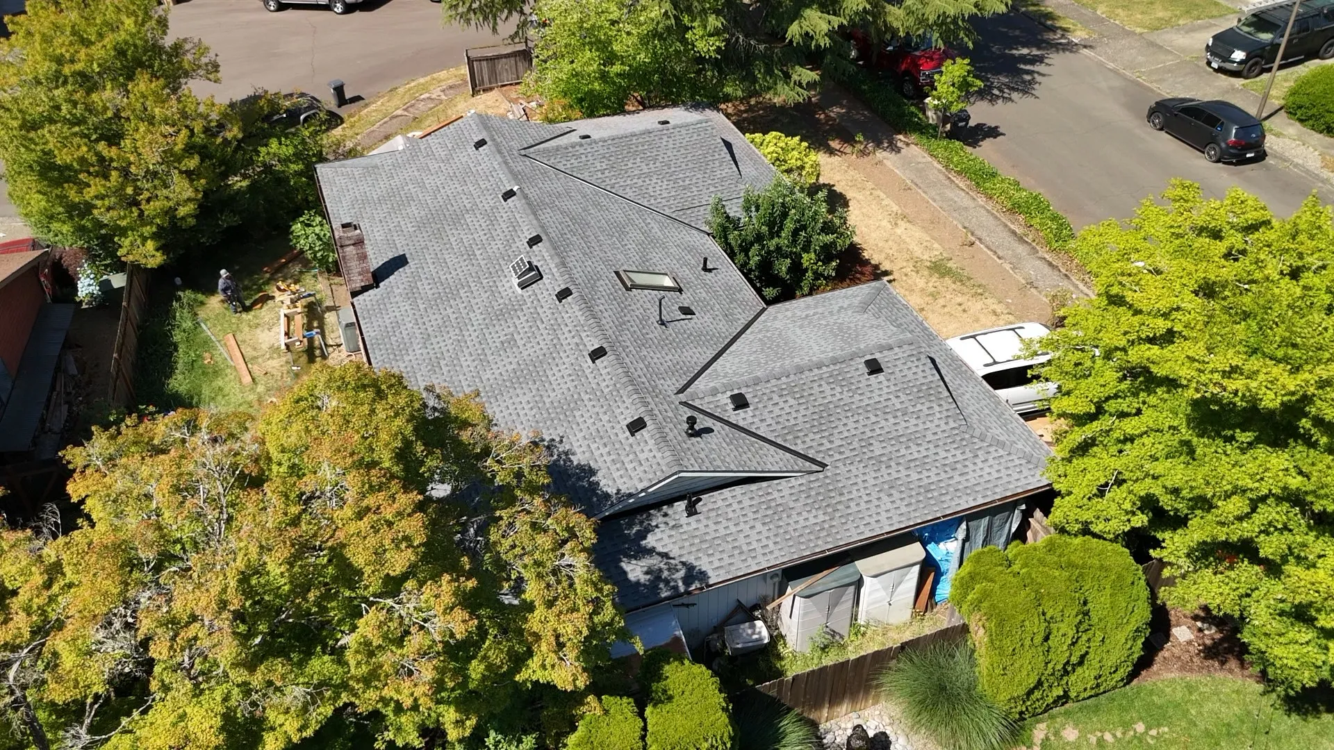 Top-down aerial view of a completed gray shingle roof with skylights and brick chimney in Tualatin, OR